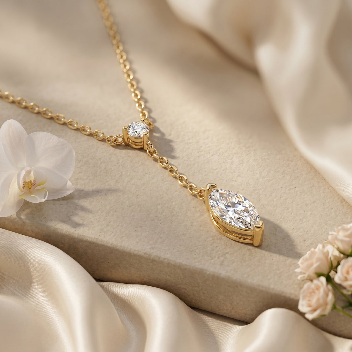 Close-up of a gold lariat necklace featuring a brilliant marquise-cut moissanite drop on silk fabric.