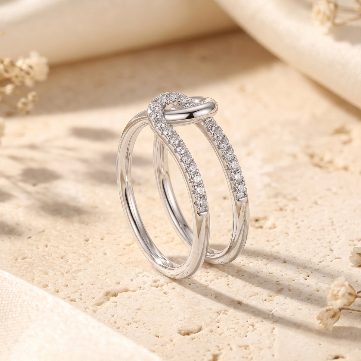 Upright angled view of the silver double-band interlocking knot ring with simulated stones on part of each band.