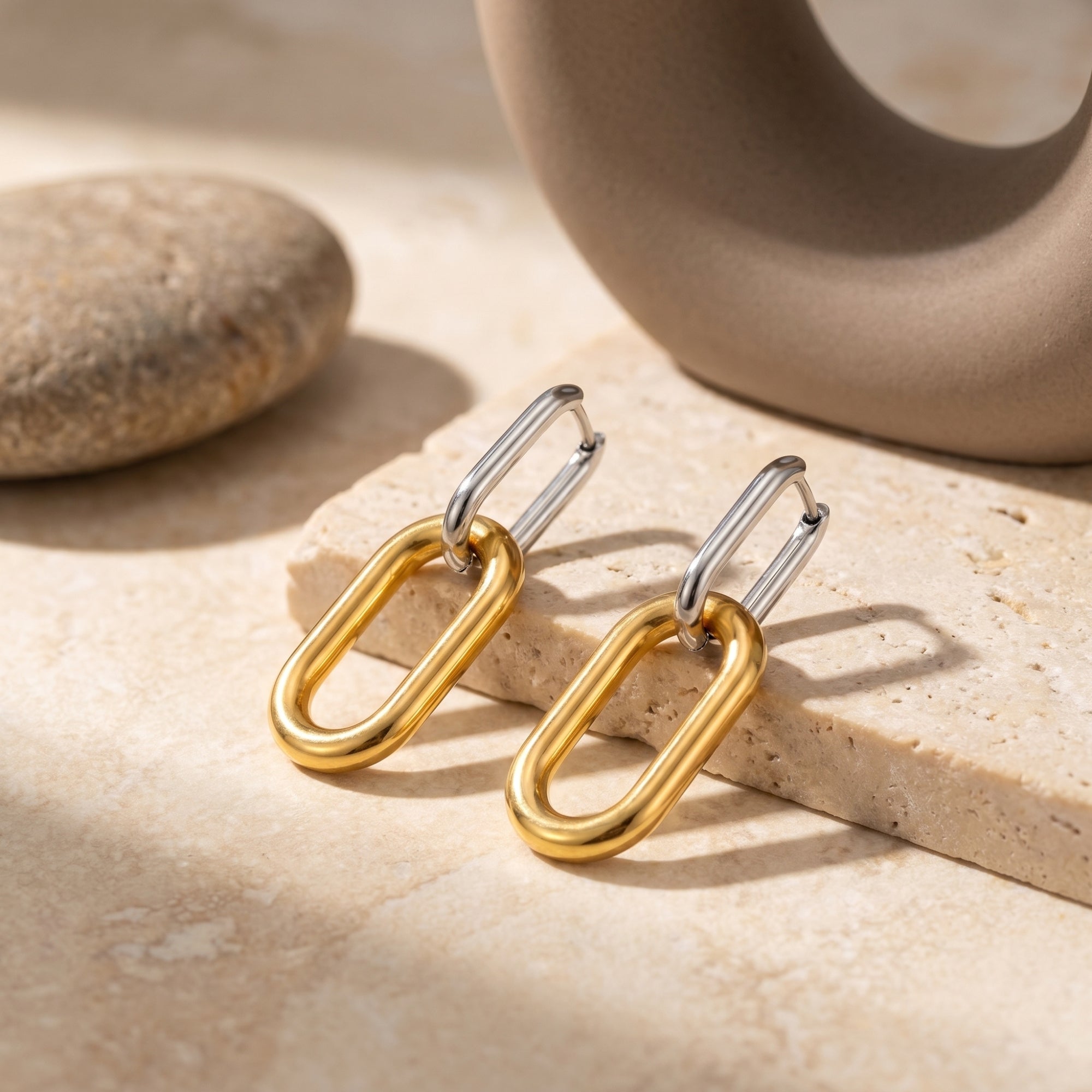 Silver and gold stainless steel drop earrings resting on a textured stone surface.