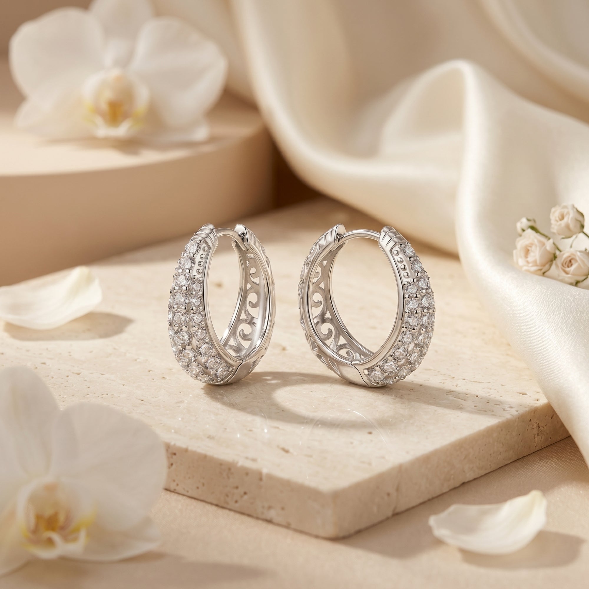 Round-cut moissanite hoop earrings on a stone surface with white flowers and silk.