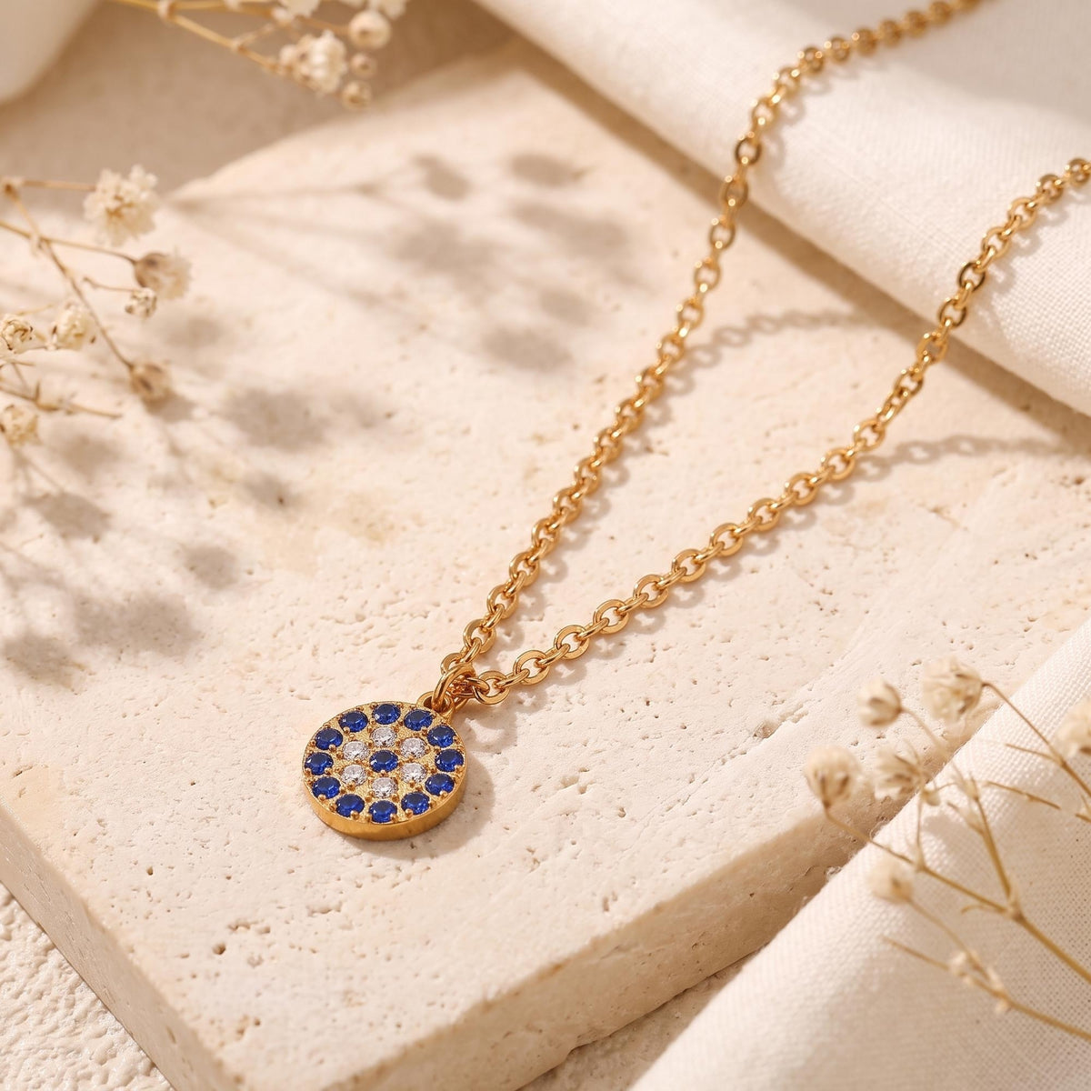 Macro view of the circular 18K gold PVD pendant with blue and white simulated sapphire pave stones.