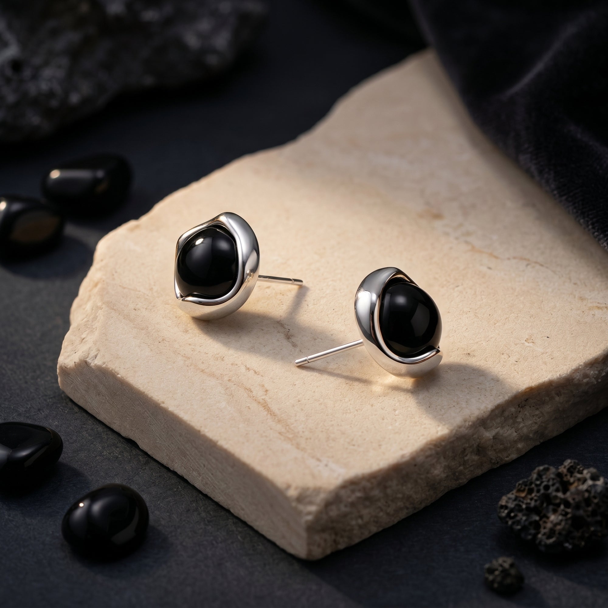 Side view of round black onyx earrings in silver settings showing the earring posts on a stone slab.