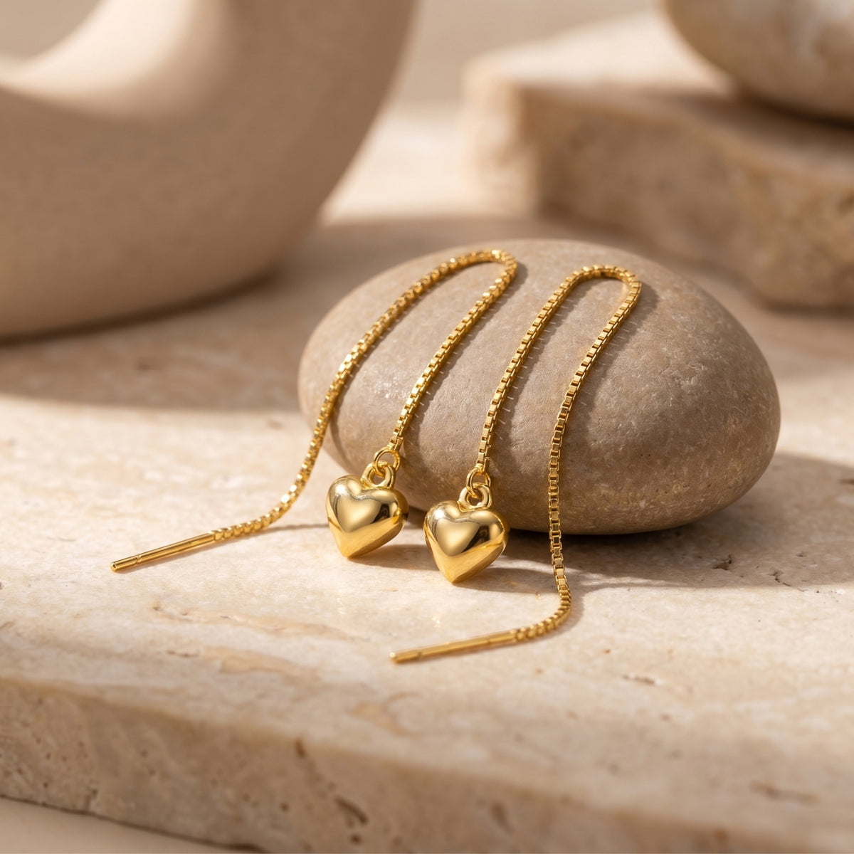 Gold heart threader earrings with polished heart charms and box chains on a smooth river stone.