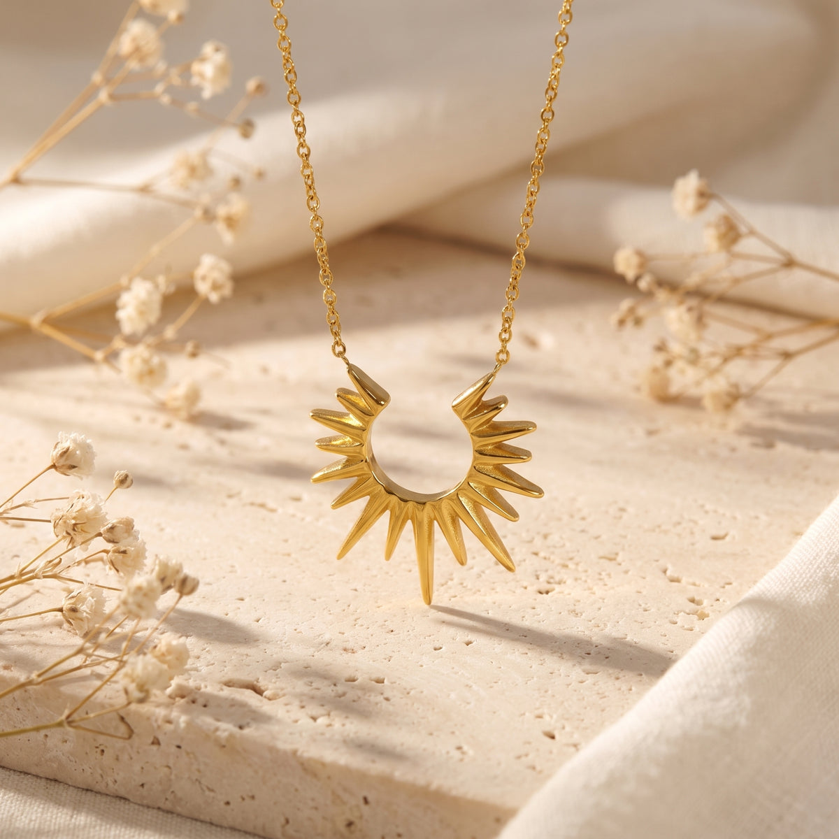 Frontal view of the gold-toned sunburst pendant hanging upright above a neutral stone surface.