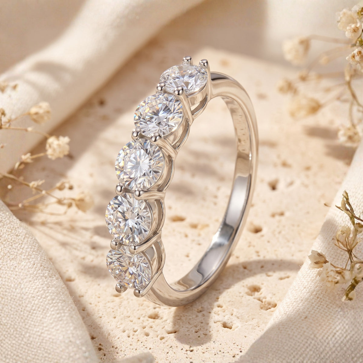 Angled side view of a silver band ring showcasing five prong-set round faceted clear stones.