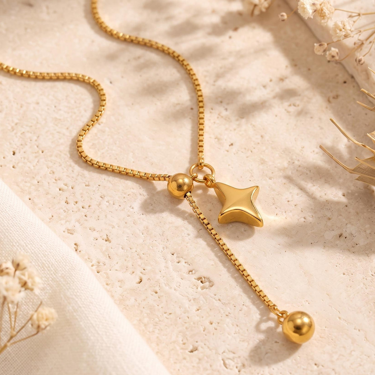 Close-up of the gold-tone four-point star charm, sliding bead, and dangling end bead on a box chain.