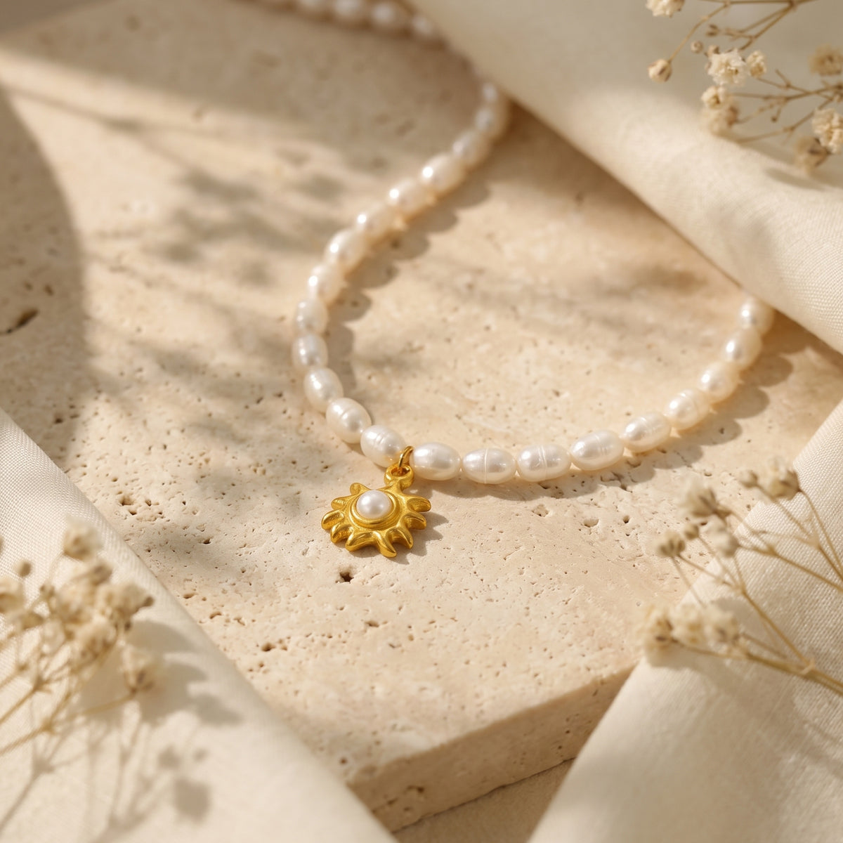 Close-up of a gold sunburst pendant and freshwater pearls on a neutral stone background with soft shadows.