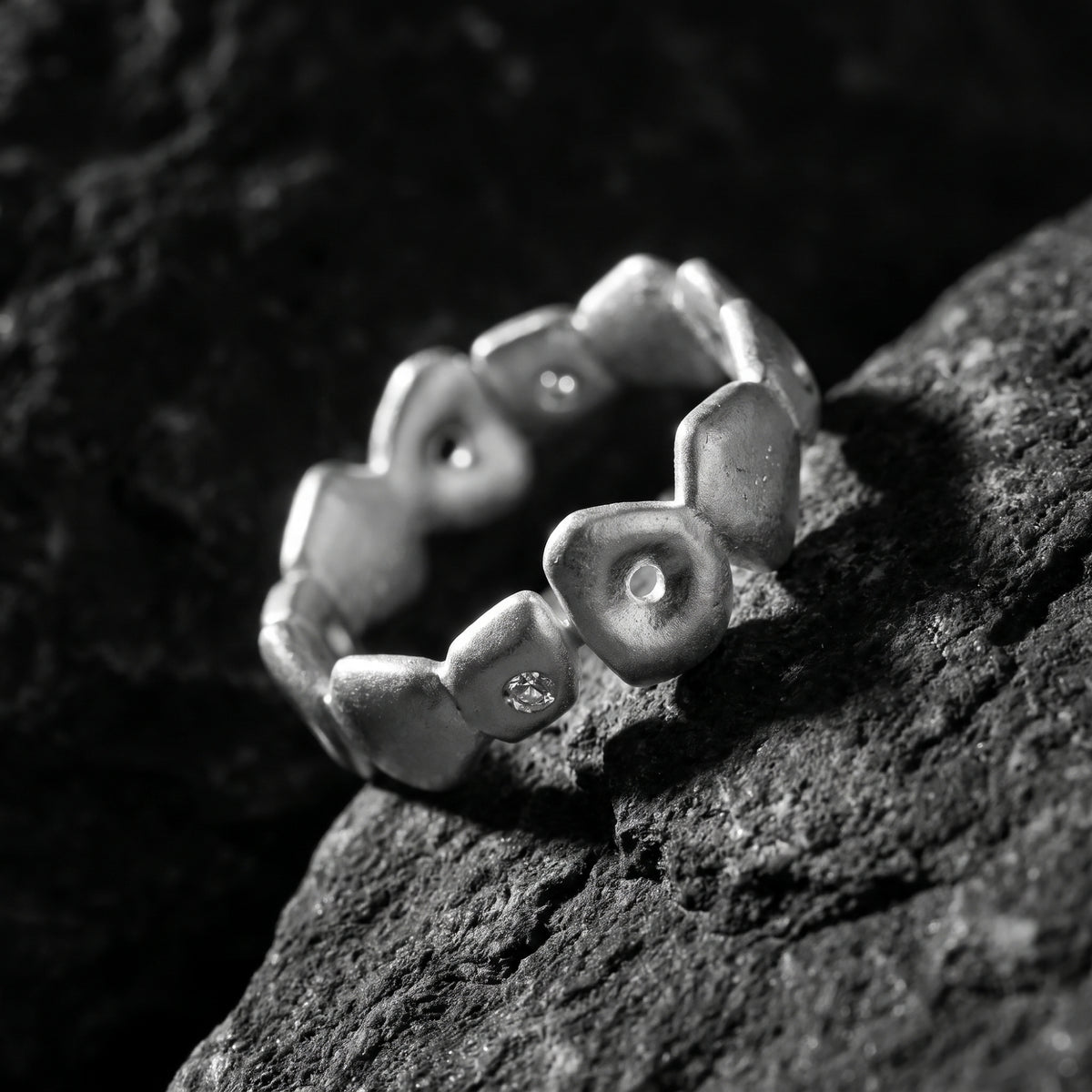 Angled close-up of the pebble open-band ring on rock, with one clear faceted accent visible.