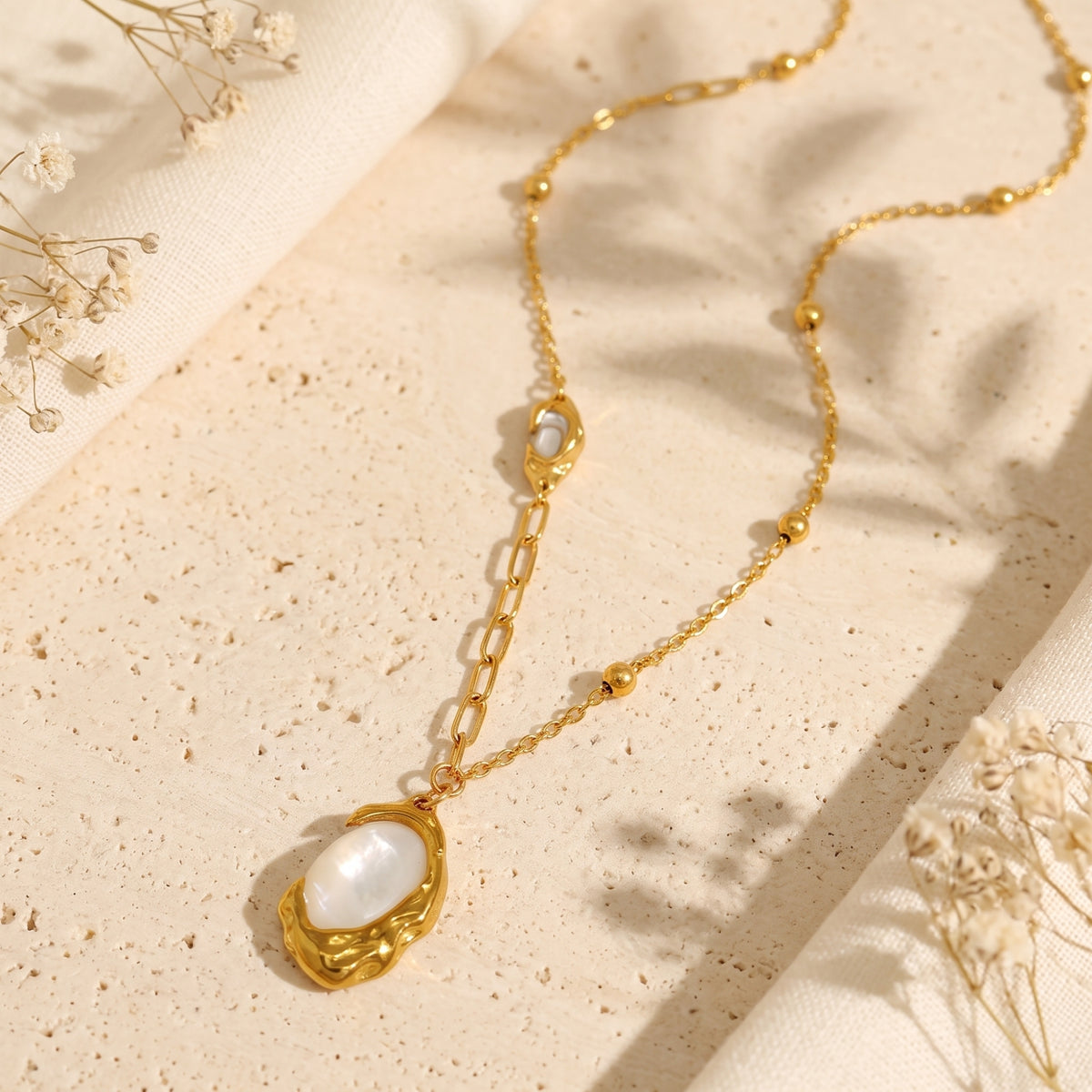Flat lay display of the gold-tone asymmetrical necklace with a molten oval mother-of-pearl pendant.