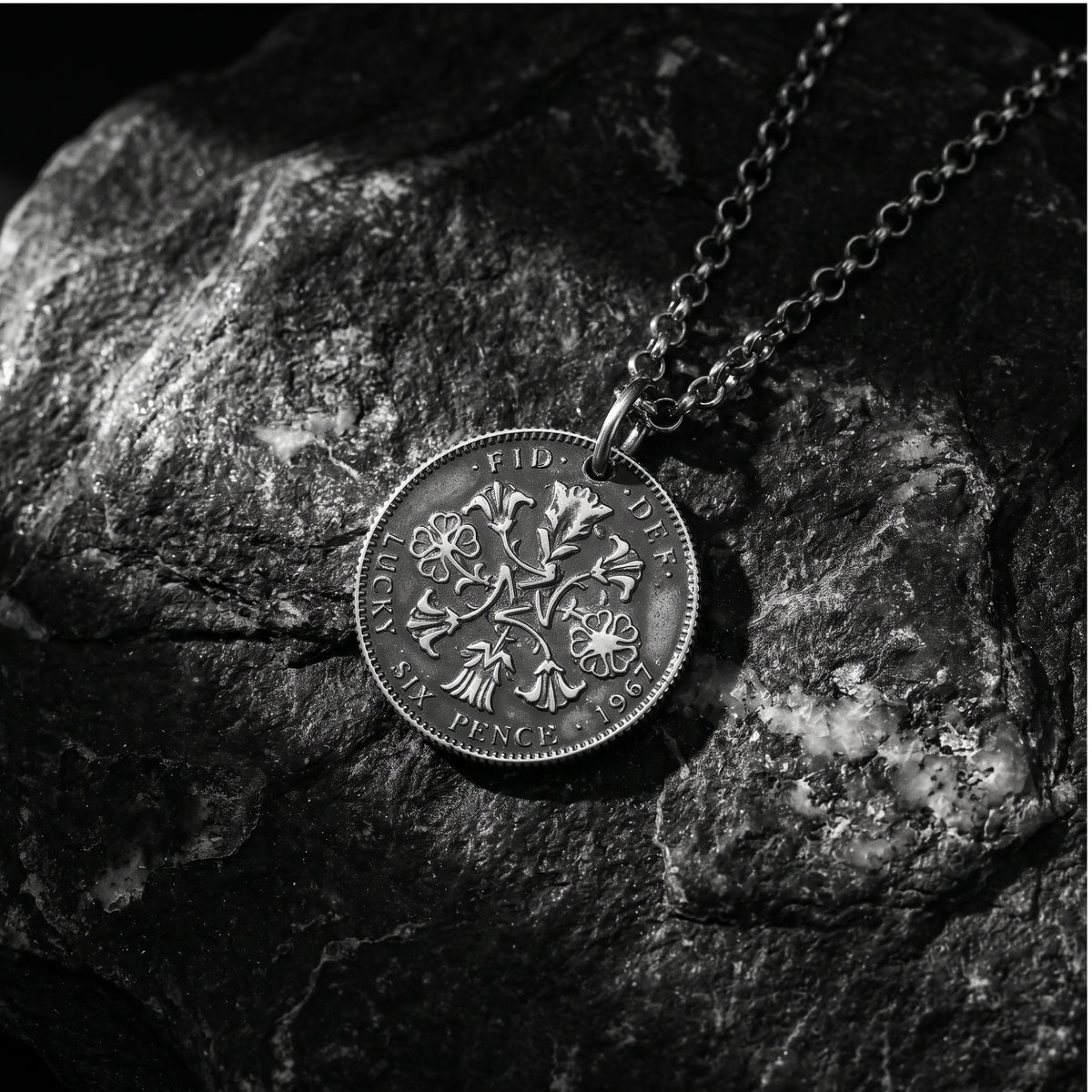 Angled close-up of the silver coin pendant and chain resting on a textured dark rock surface.