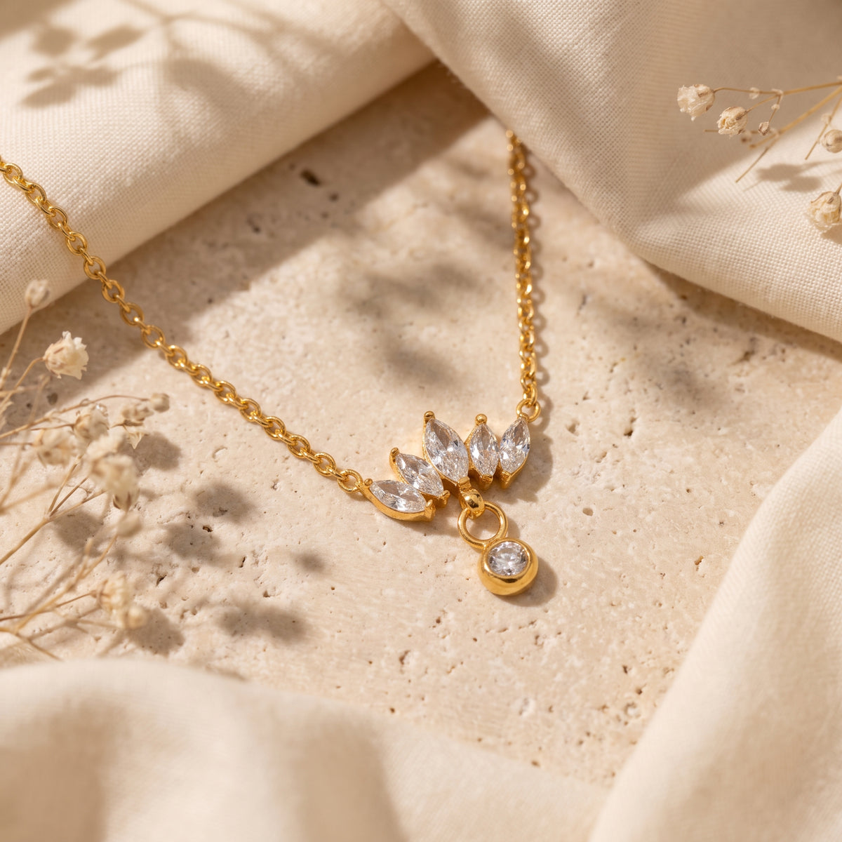 Angled view of the gold-tone lotus marquise drop necklace resting on textured stone surrounded by fabric.