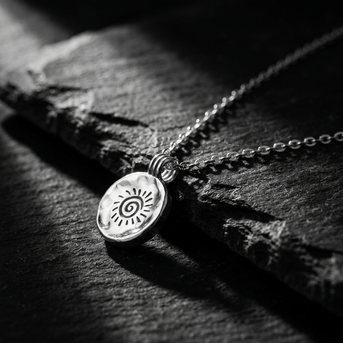 Angled close-up of the silver spiral sunburst pendant resting on a dark slate surface.