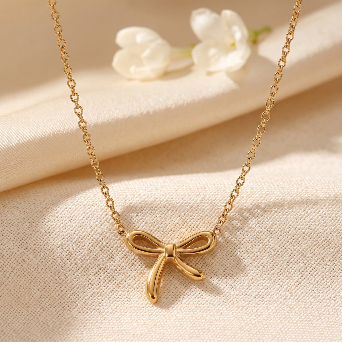 Close-up of the sculpted gold-tone ribbon bow pendant on a fine link chain.