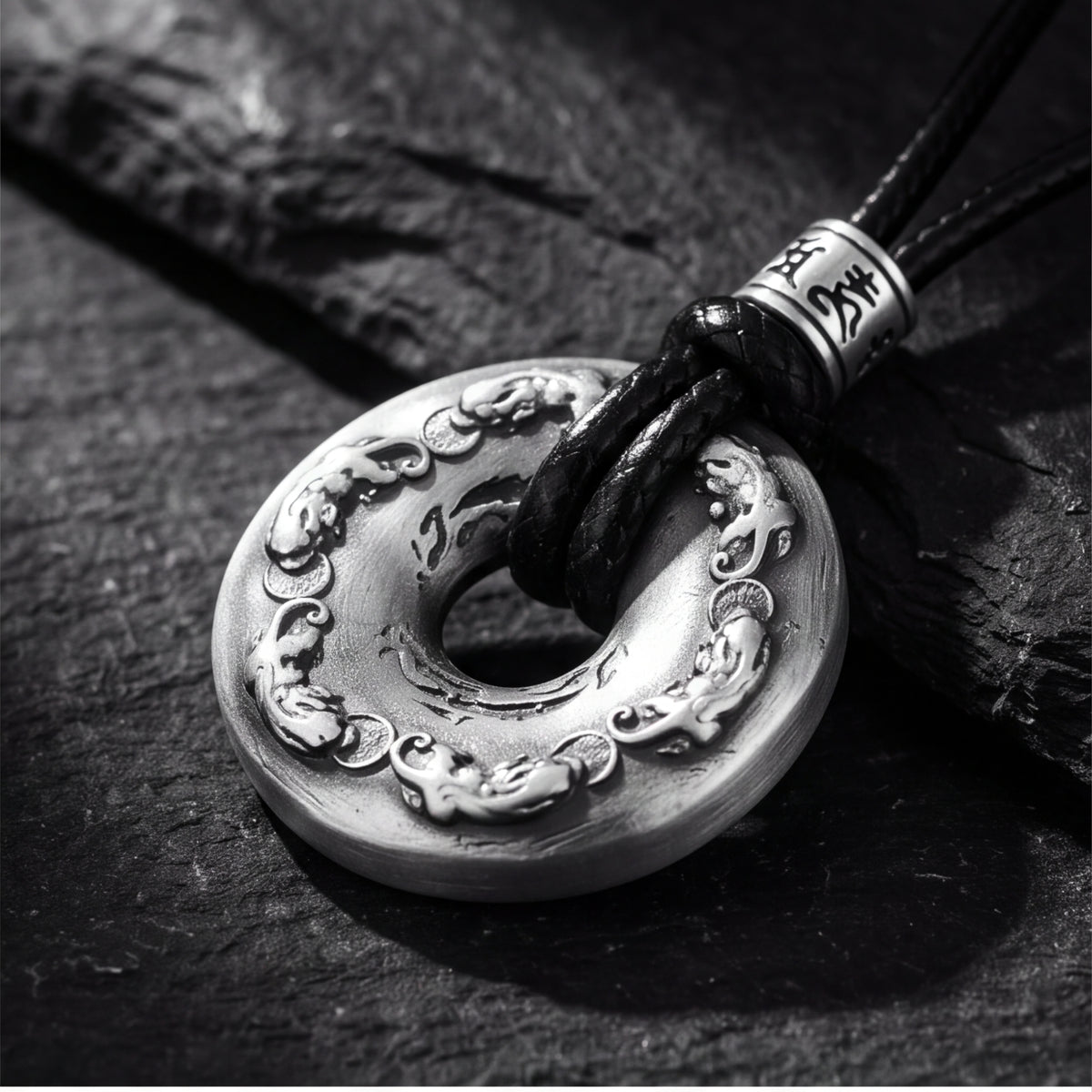 Angled close-up of the antiqued silver disc pendant resting on dark stone, showing intricate carvings.