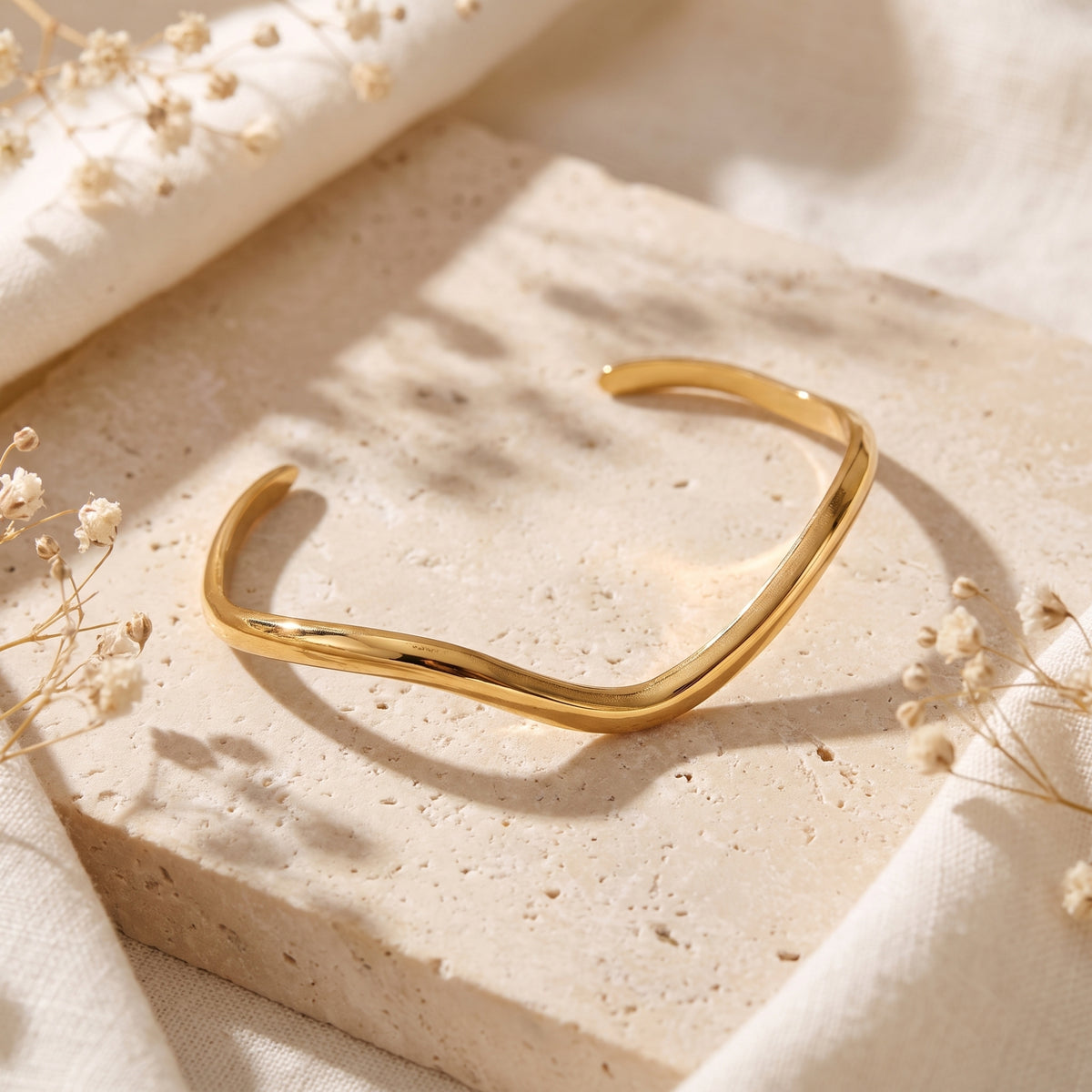 High-angle view of the open gold-tone wave cuff resting flat on a porous stone block.