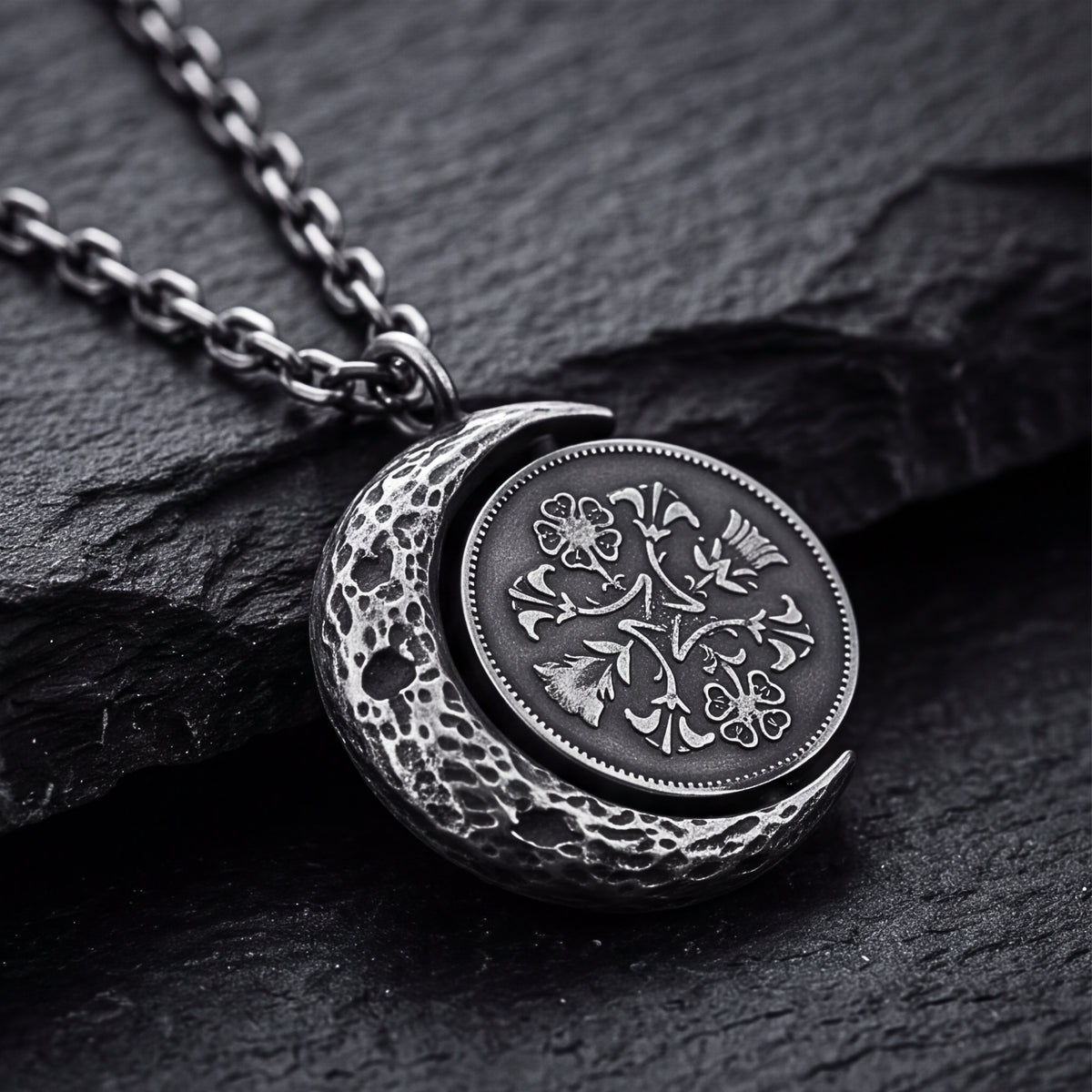 Angled close-up of the silver lunar coin pendant on dark slate, showing the textured crescent frame and floral coin center.