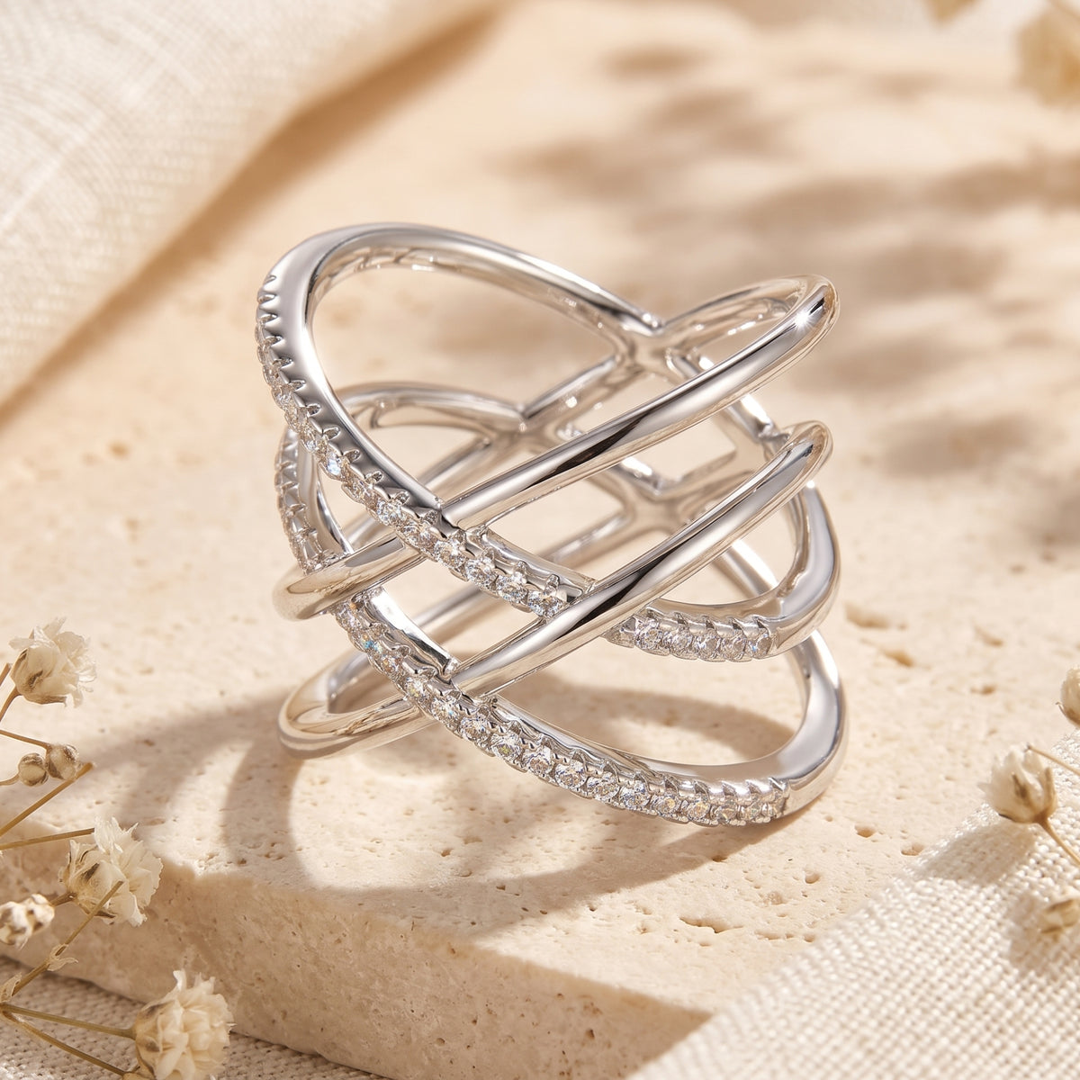 Angled view of a silver crossover ring showing its openwork woven bands and pavé stone details.