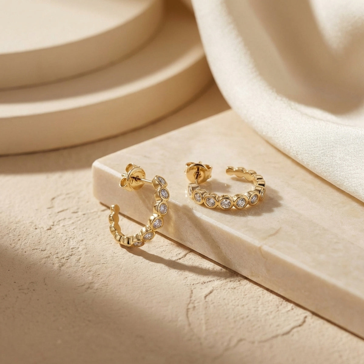 Gold-tone moissanite hoop earrings displayed on a beige stone block, with posts and butterfly backs visible.