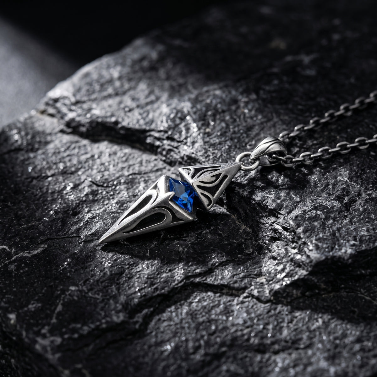 Angled close-up of the silver pendant lying diagonally on a rough, dark rock surface.