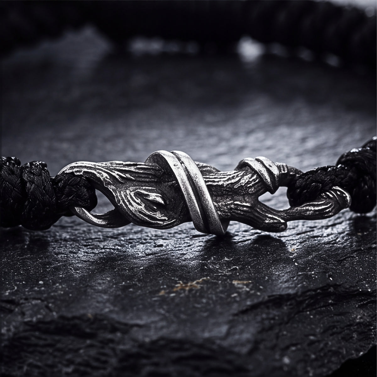 Close-up of the branch-textured silver hook clasp connecting the black woven cord bracelet on a slate surface.