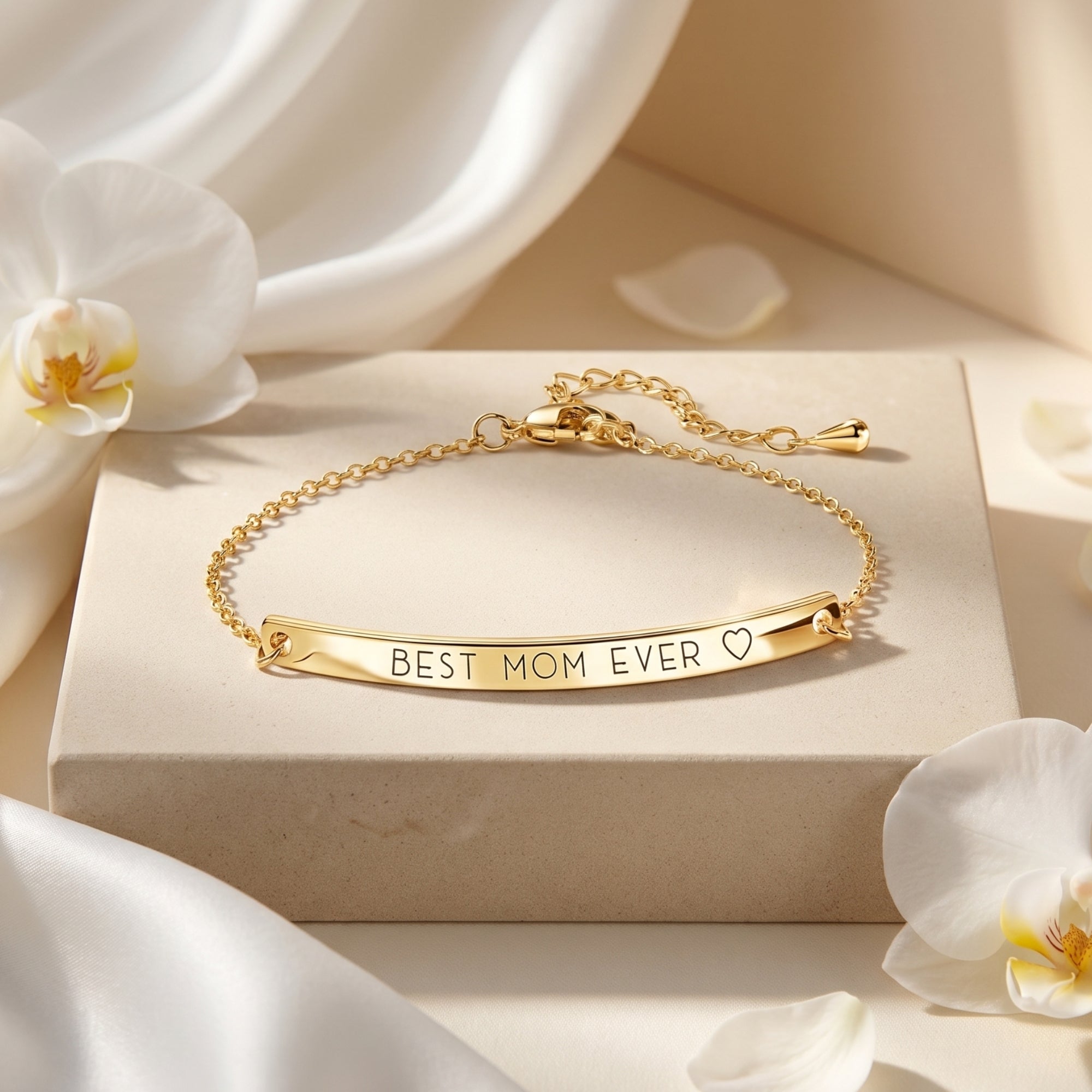 Gold Eleanor Bar Bracelet with BEST MOM EVER engraving displayed on a stone block with white orchids.