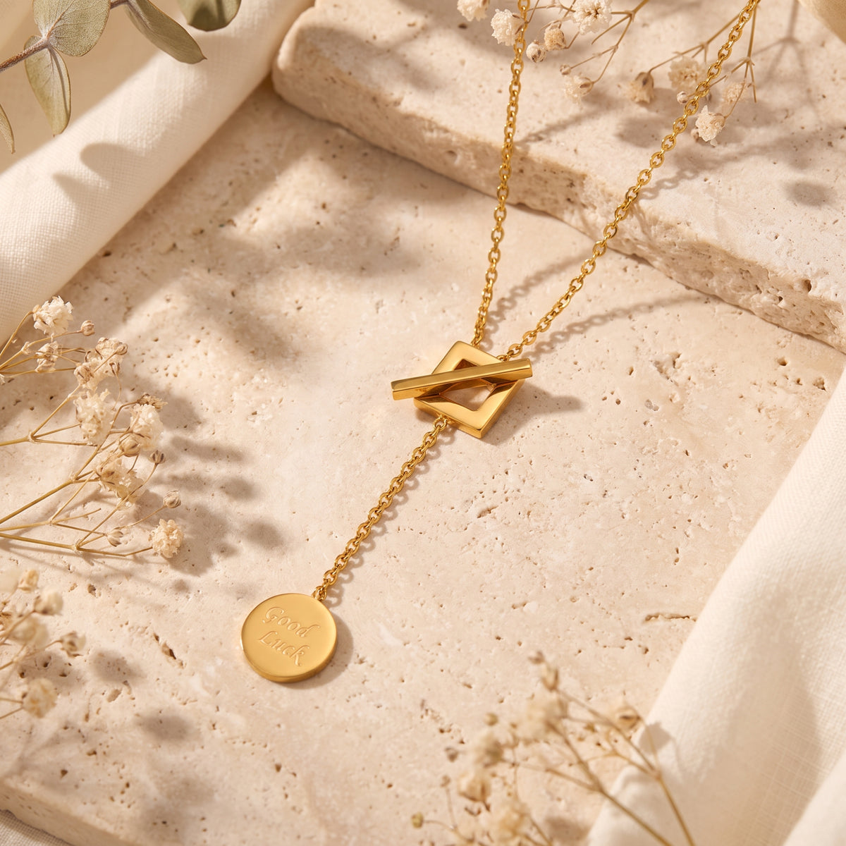 Top-down view of gold-tone lariat necklace featuring square toggle centerpiece and engraved coin charm.