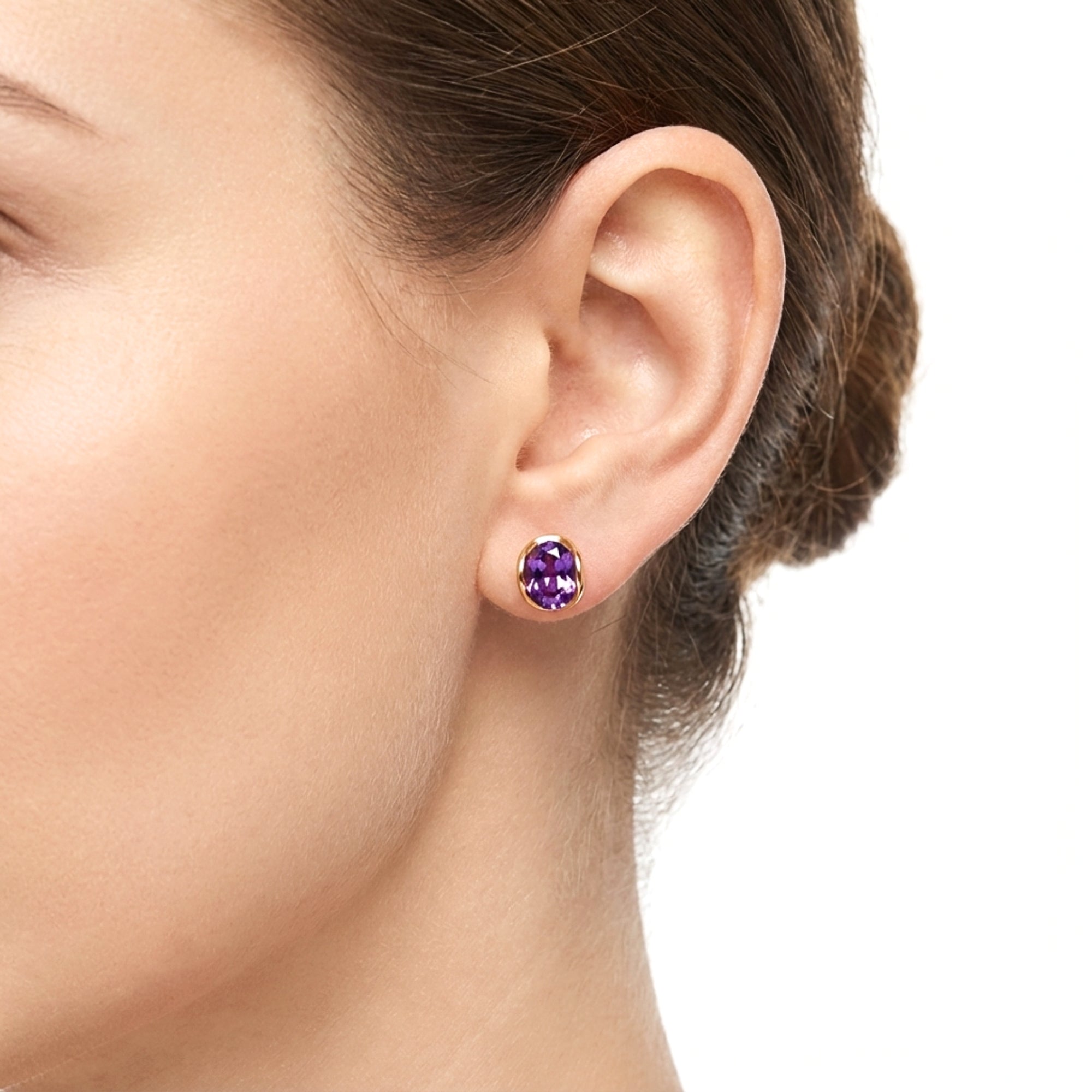 Close-up of a model wearing an 18K gold vermeil hoop earring with an oval cut simulated amethyst stone.
