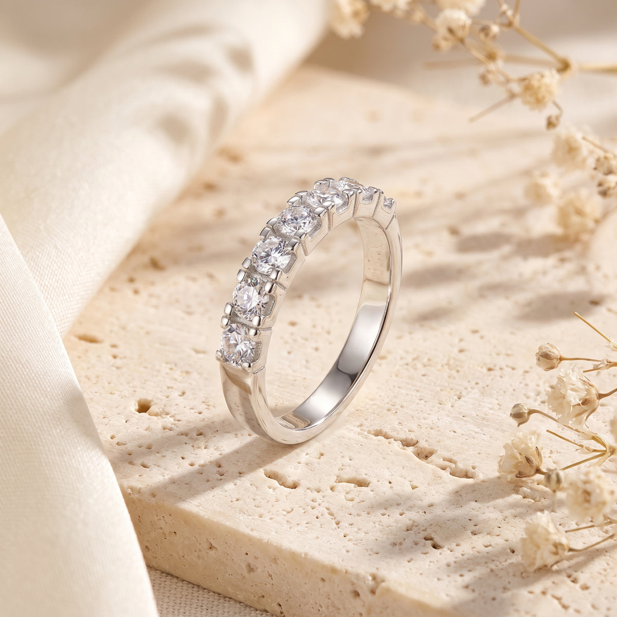 Angled view of the silver Evadienne eternity ring featuring round-cut simulated diamonds on a textured stone background.