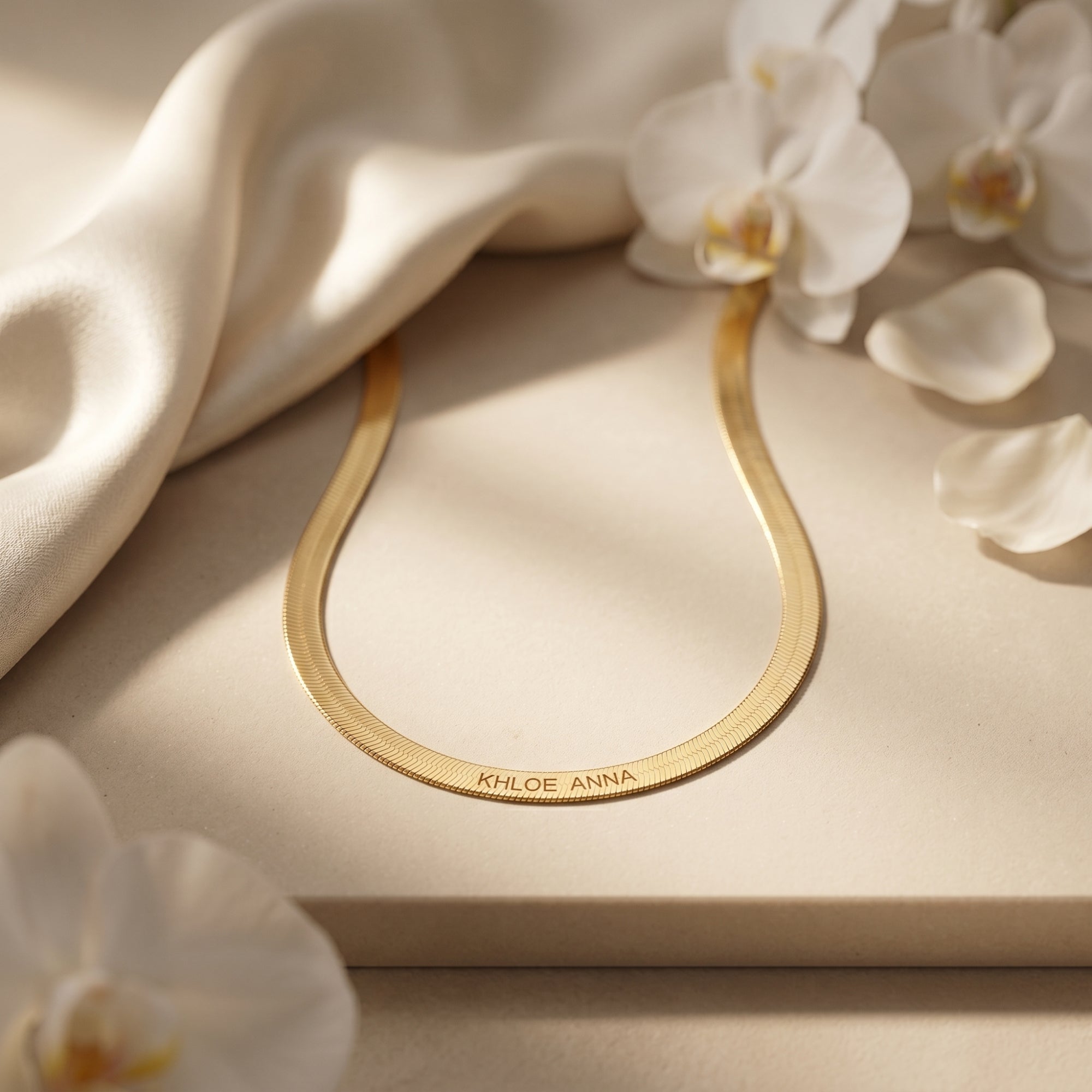 Close-up of custom name engraving on 18K gold finish herringbone necklace with orchids.