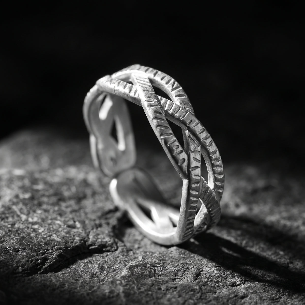 Angled view of a silver textured interlocking open ring standing upright on dark rock.