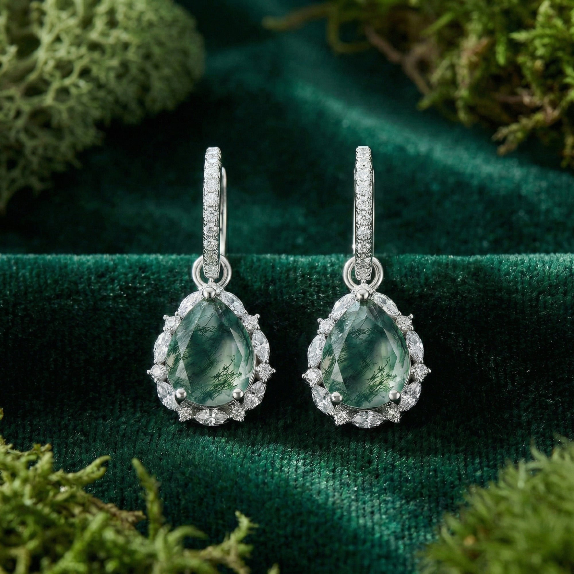 Close-up of teardrop moss agate leverback earrings in sterling silver with a sparkling halo on green velvet.