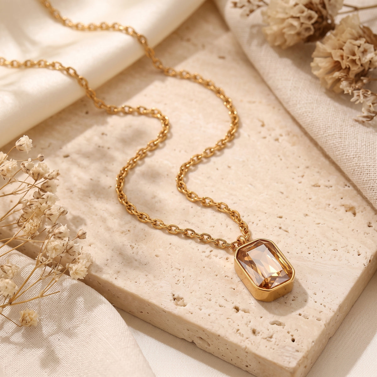 Gold-tone necklace with an emerald-cut golden-yellow simulated citrine pendant displayed on textured travertine.
