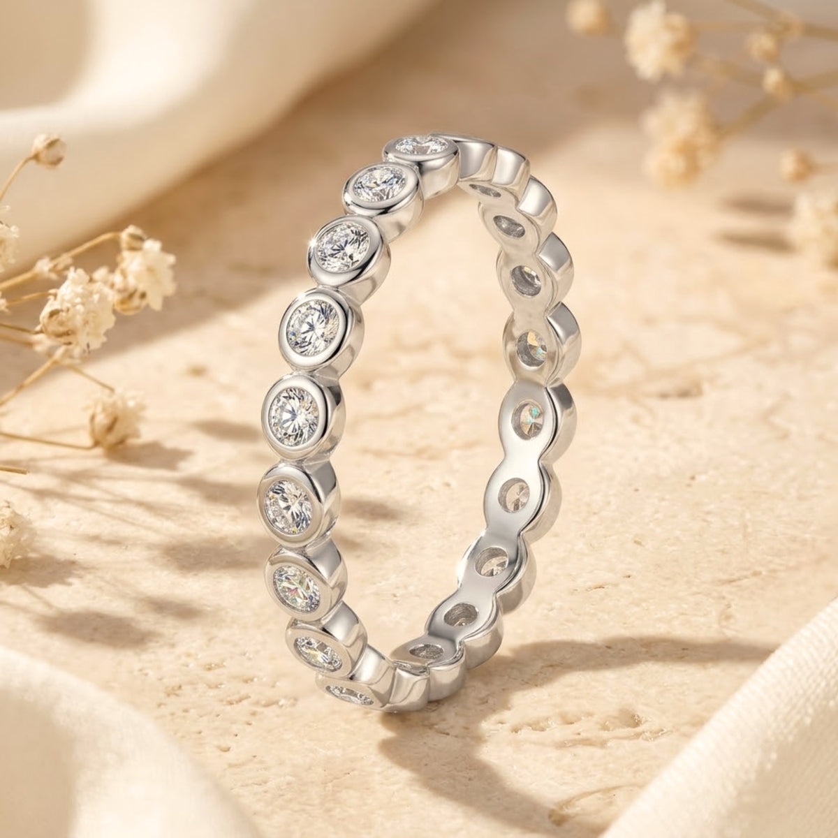 Silver eternity ring standing vertically on a stone block, displaying bezel-set round gems.