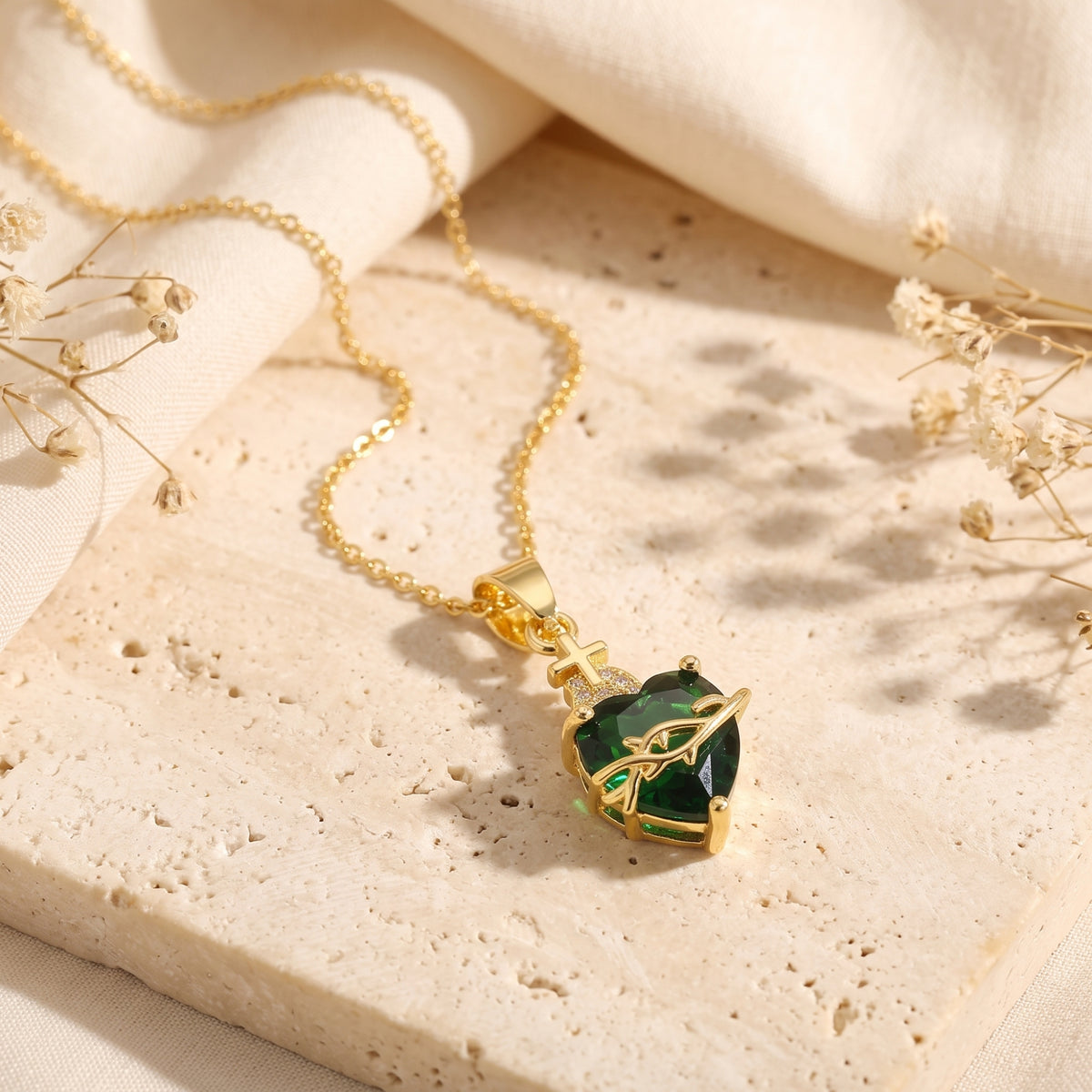 Green heart crystal sacred heart pendant necklace with coiled gold chain on a travertine surface.