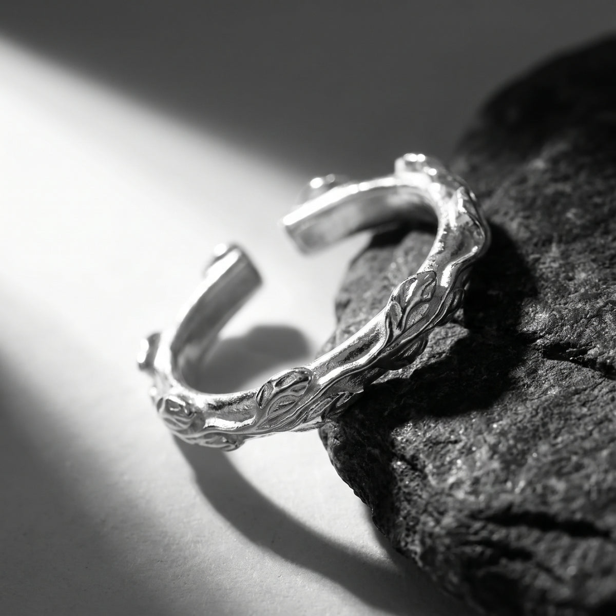Top-angled view showing the open gap and carved foliage pattern of the silver band ring on dark rock.