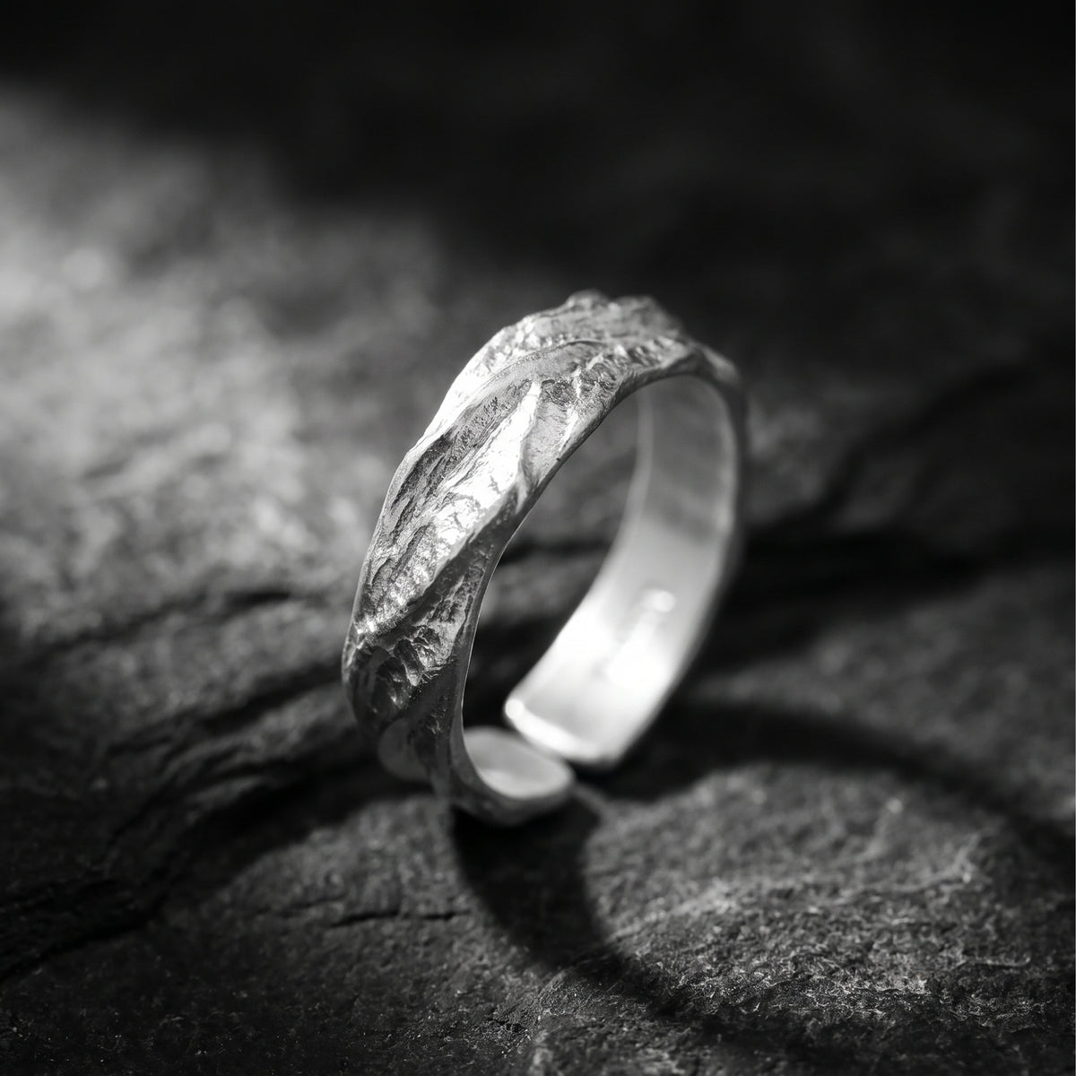 Angled close-up of a textured fine silver open band ring standing on rough rock, showing its gap and inner surface.