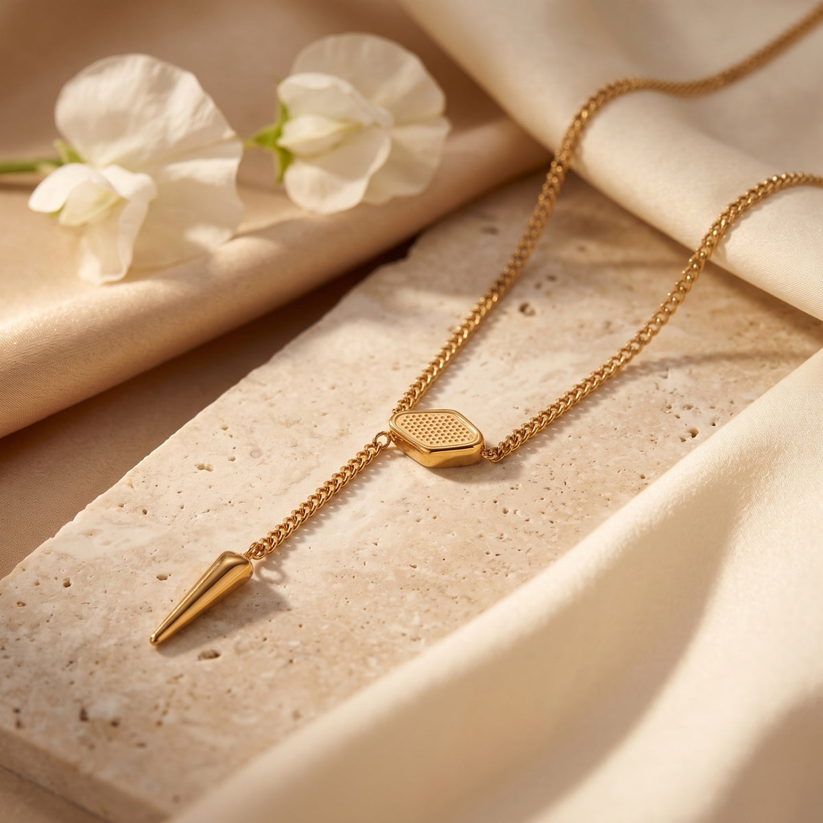 Detail shot of the gold hexagonal slider and polished spike pendant on a textured stone.