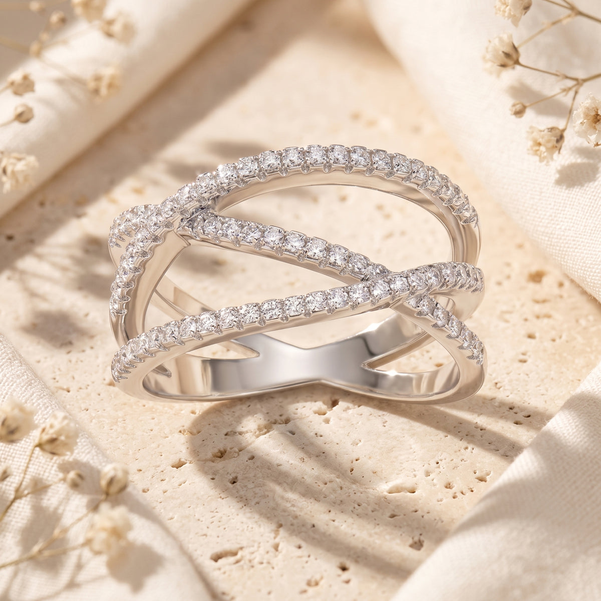 Angled close-up of a silver crossover ring with crisscrossing bands lined with clear pave stones.