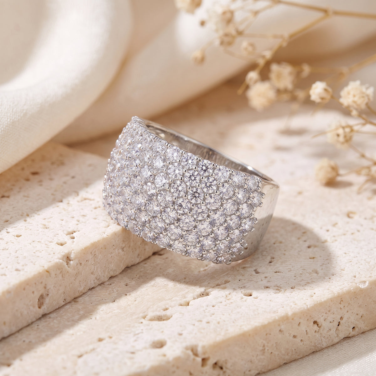 Close-up of the wide silver multi-row pave band resting on a light travertine stone surface.