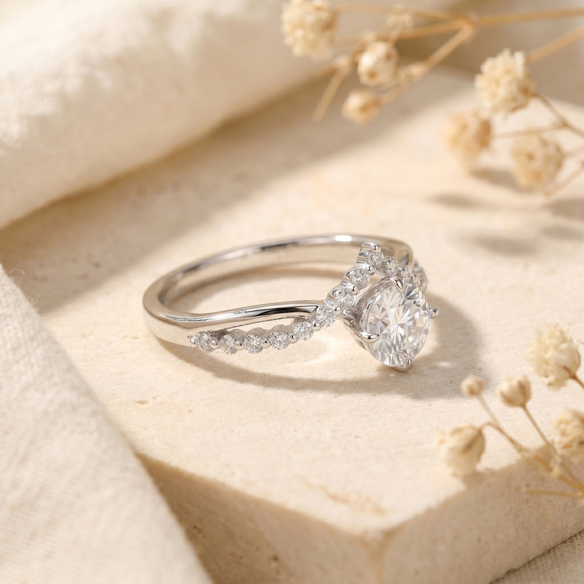 Angled view of the silver Caladienne round moissanite ring highlighting the arched crown setting on a stone surface.