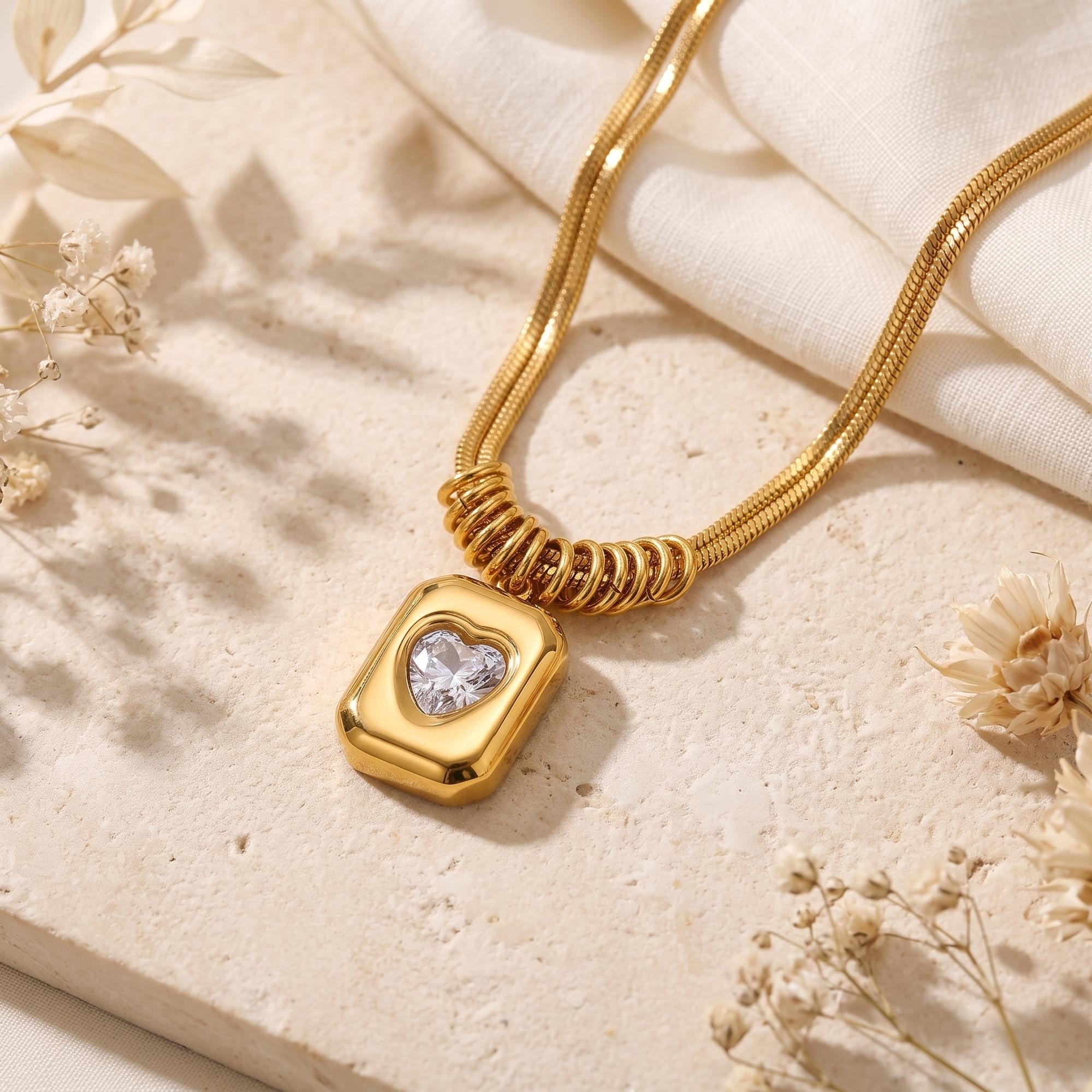 Close-up of the gold rectangular pendant and heart-cut simulated diamond on a textured stone background.