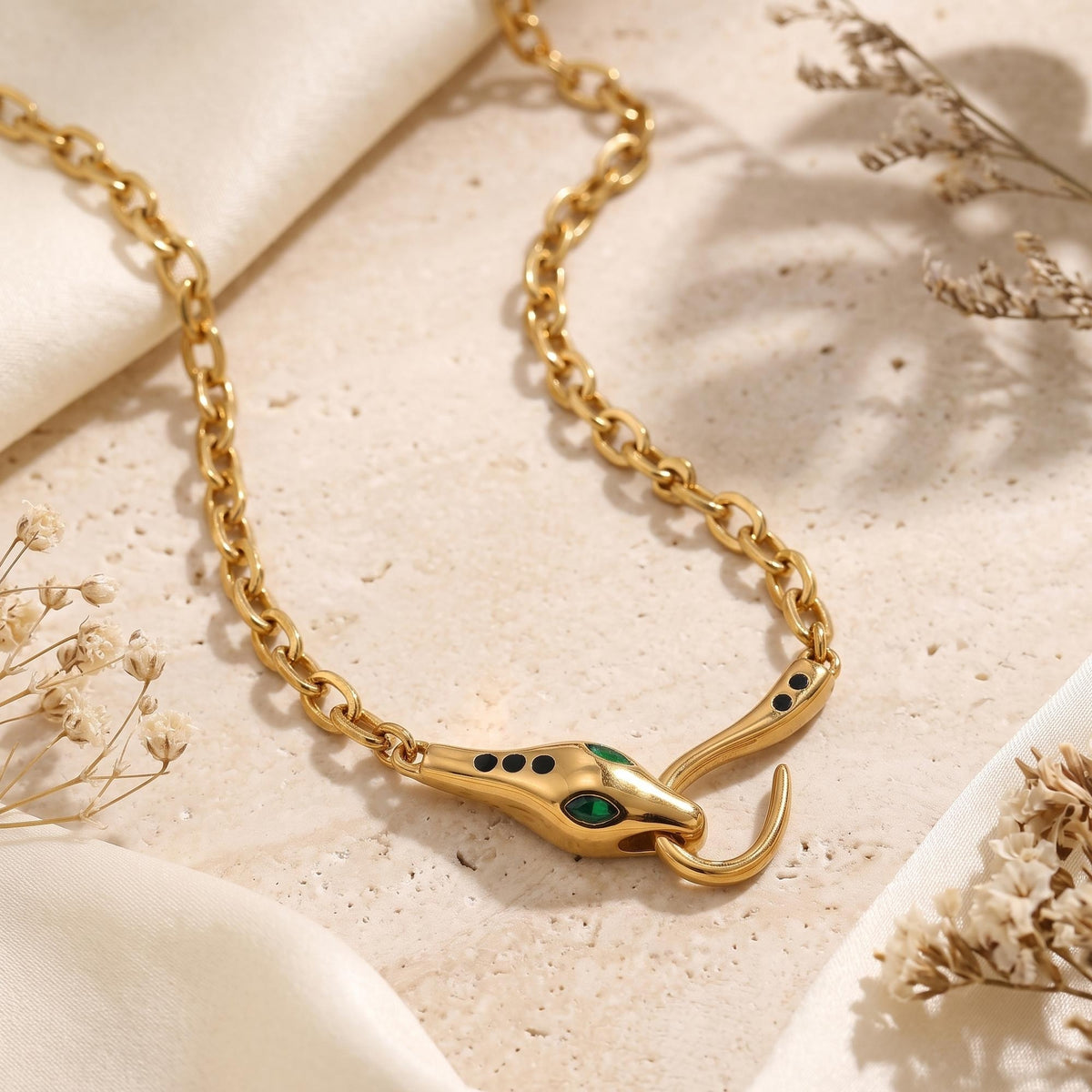 Macro view of the 18K gold PVD snake clasp with green stone eyes and black accents on a chunky link chain.