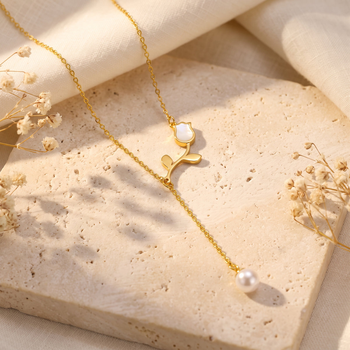 Flat lay of the gold tulip lariat necklace with pearl drop resting on a textured beige stone slab.
