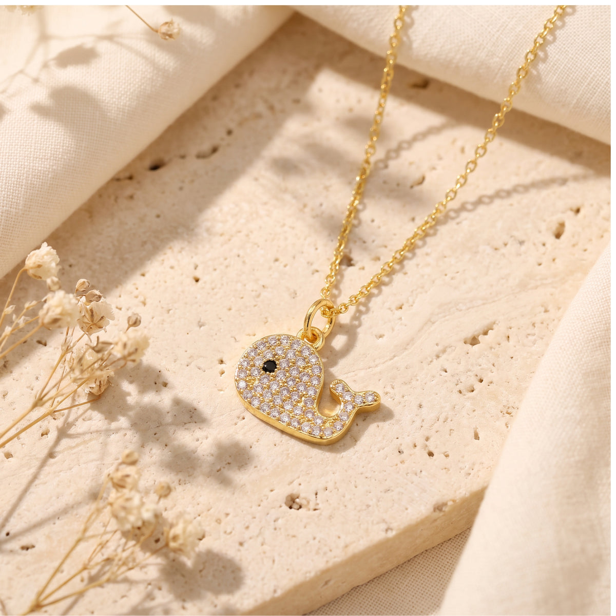 Top-down view of the crystal pave whale pendant resting flat on a beige stone surface.