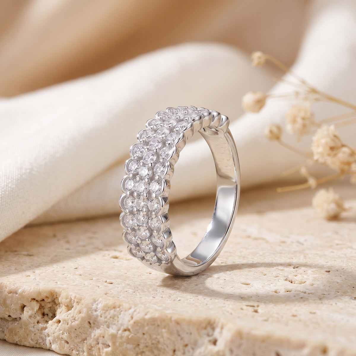 Angled side view of the silver scalloped triple-row clear-stone ring standing upright on a stone slab.