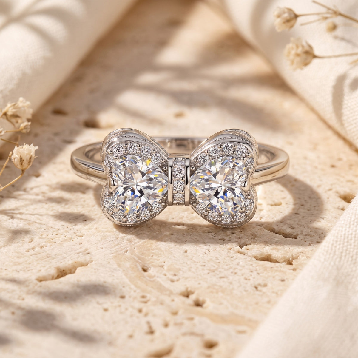 Front-facing silver bow ring with two heart-shaped stones, halo accents, and small stones between them.