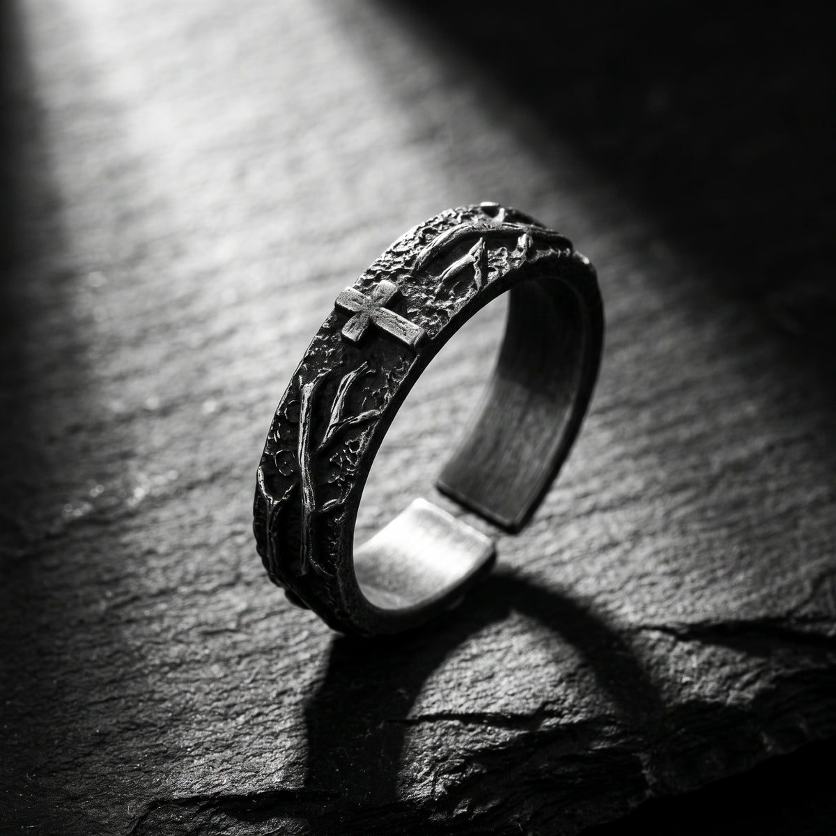 Angled close-up of the oxidized silver open-band ring showing its cross and thorn relief on dark stone
