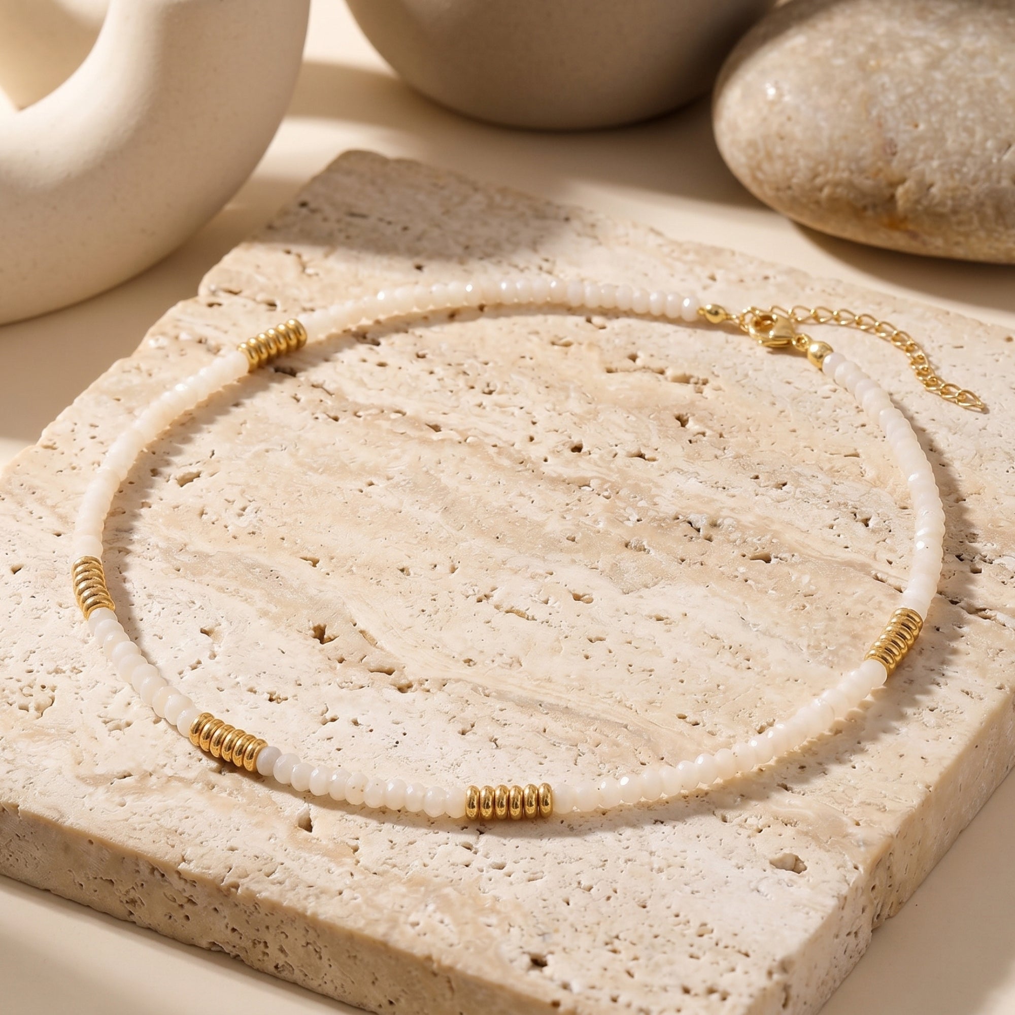 Natural white quartz beaded necklace with gold stainless steel accents displayed on a stone slab.