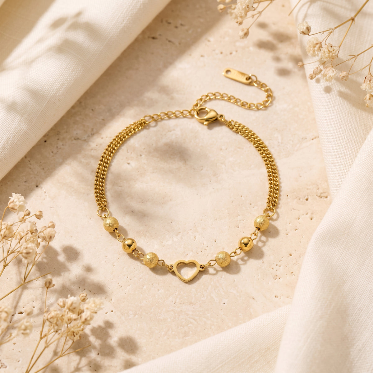 Overhead view of the gold-tone heart station bracelet arranged in a curve on a stone slab between fabric folds.