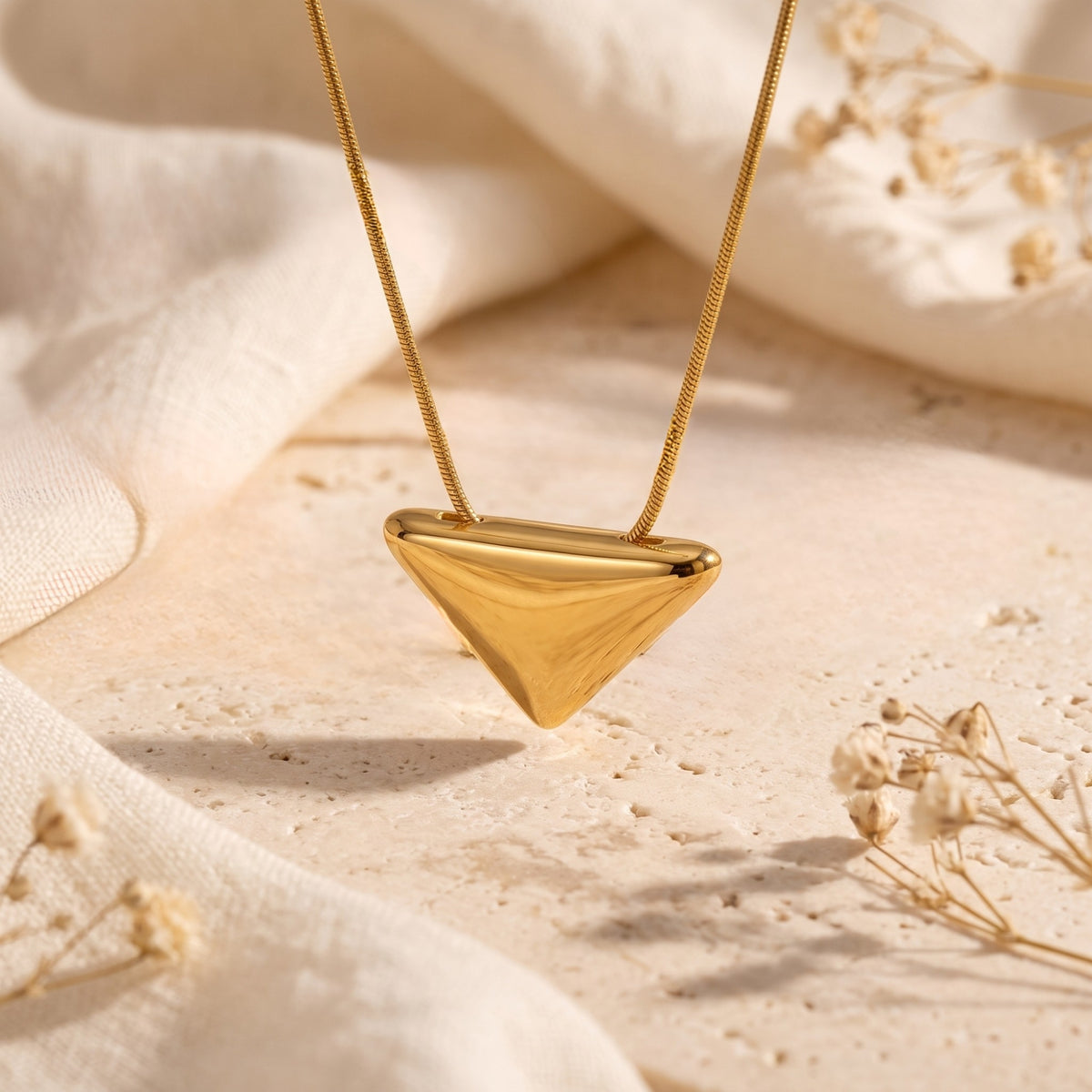 Close-up of the smooth, gold-tone triangle pendant suspended over a stone backdrop.